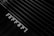 A close-up view of a Ferrari logo on a sleek, black surface with a grille-like pattern in the background. The composition highlights the luxury branding and design details, with an emphasis on texture and contrast.