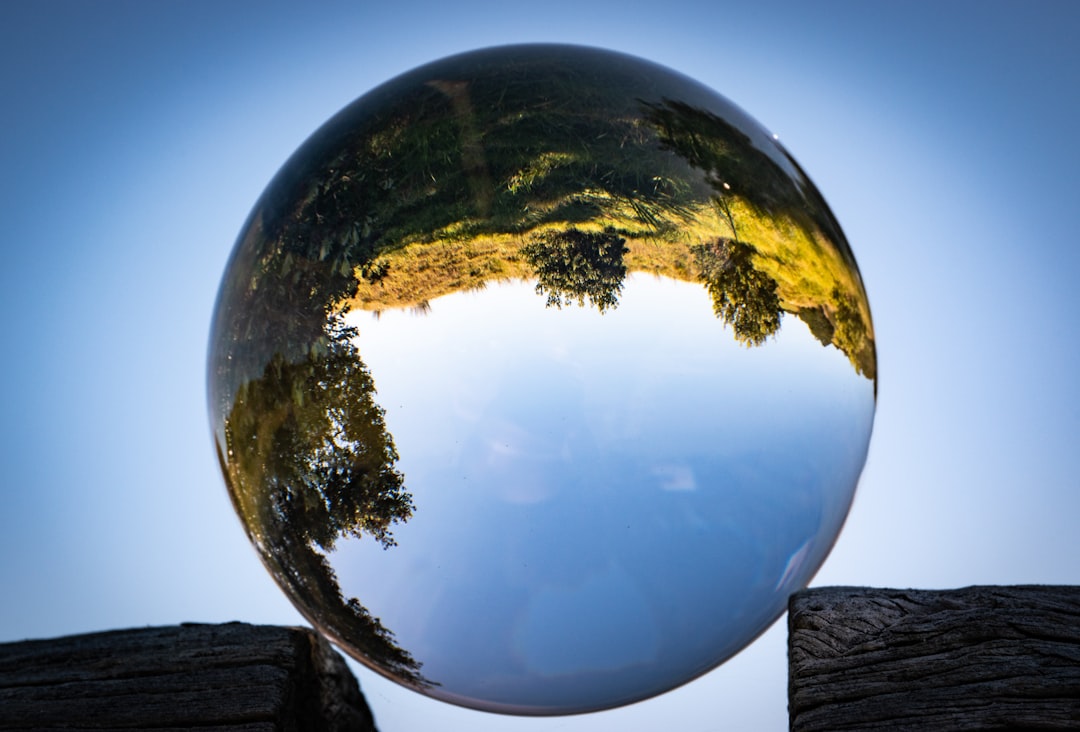 Photo by Look Up Look Down Photography of an optical glass sphere balanced in the gap of a rock formation. In the sphere, you can see grasses and trees against the backdrop of a blue sky.