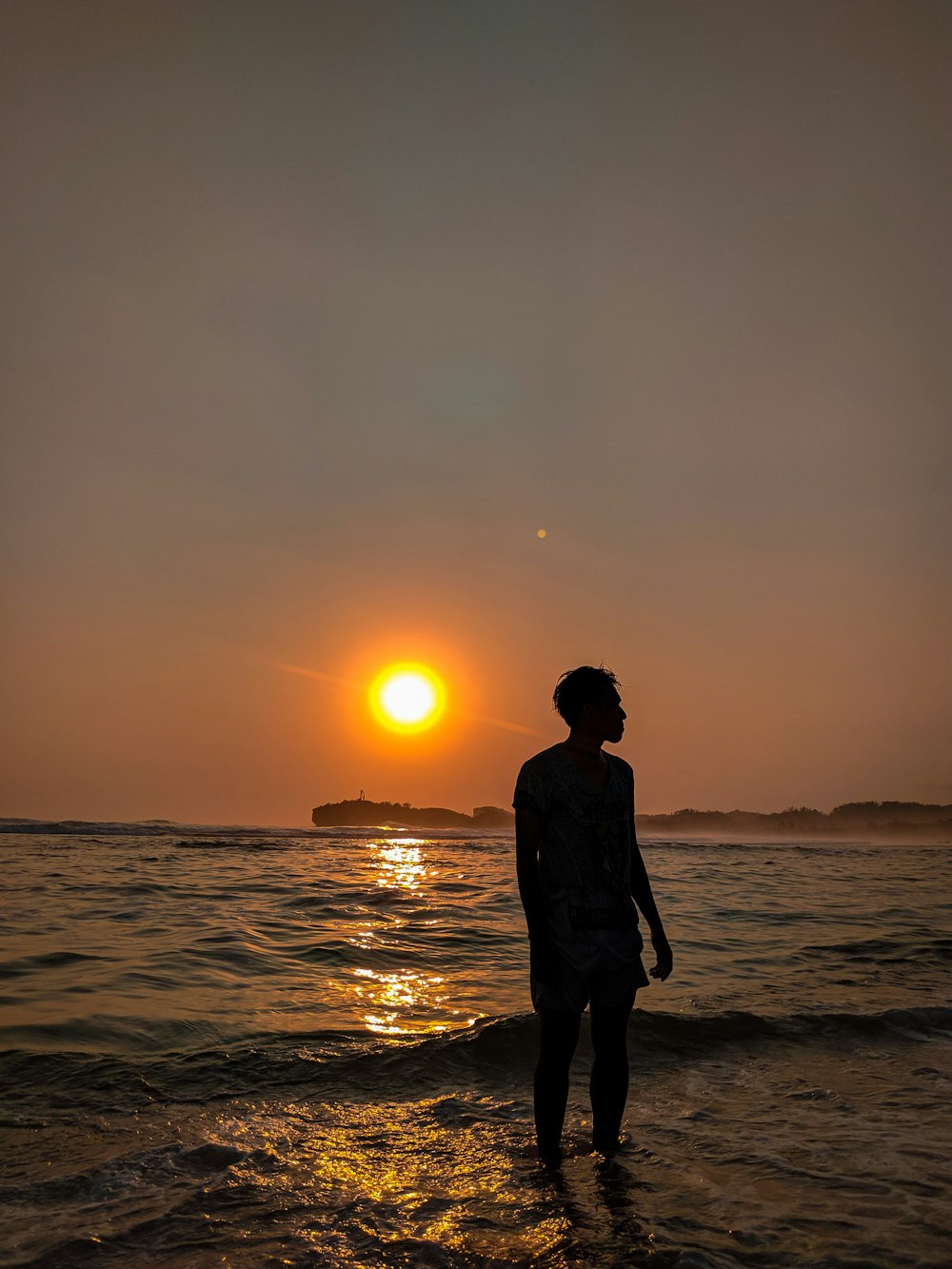 Hombre de pie en la orilla del mar durante la puesta del sol