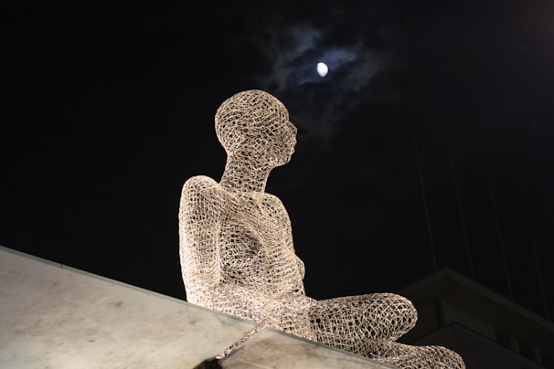 Abstract sculpture made of intertwined wires and glowing elements displayed outdoors at dusk