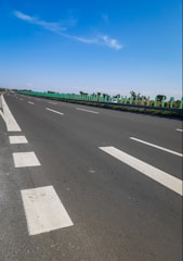 A freshly paved asphalt road with bright white lane markings under a clear blue sky.
