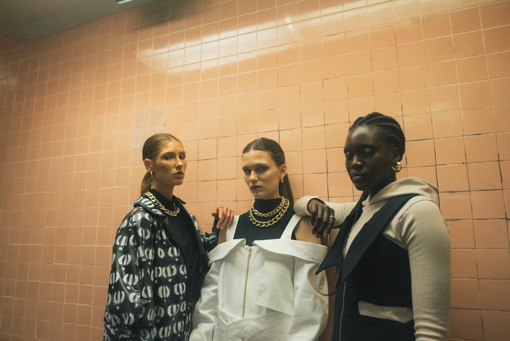 three women standing beside brown wall