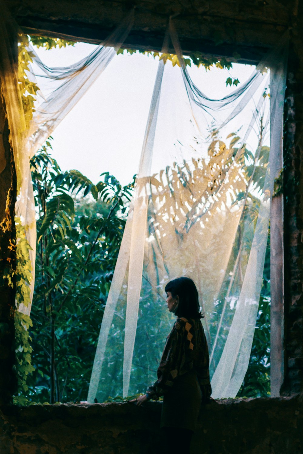 薄手のカーテンで正面の窓に立つ女性