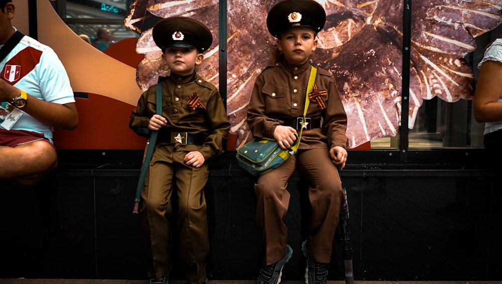two boys in brown police uniform sitting near wall