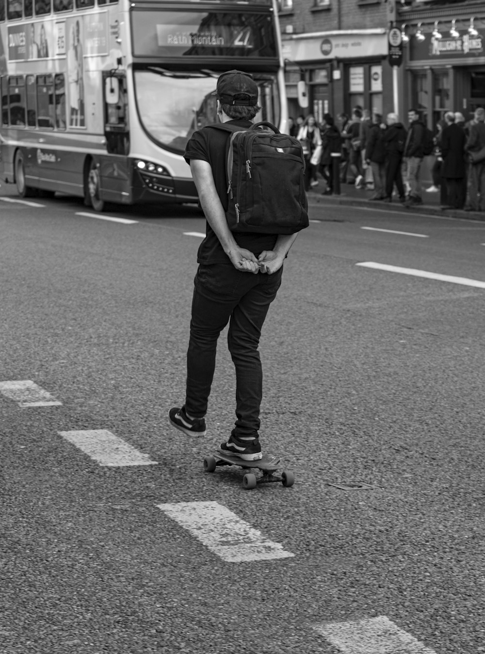 Homem andando de skate na estrada perto de ônibus em escala de cinza