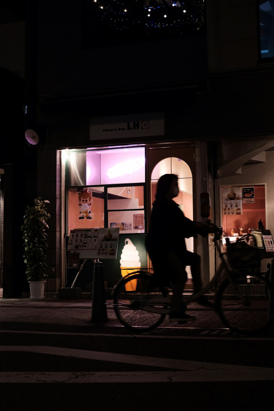 woman riding bicycle passing building with light turned on