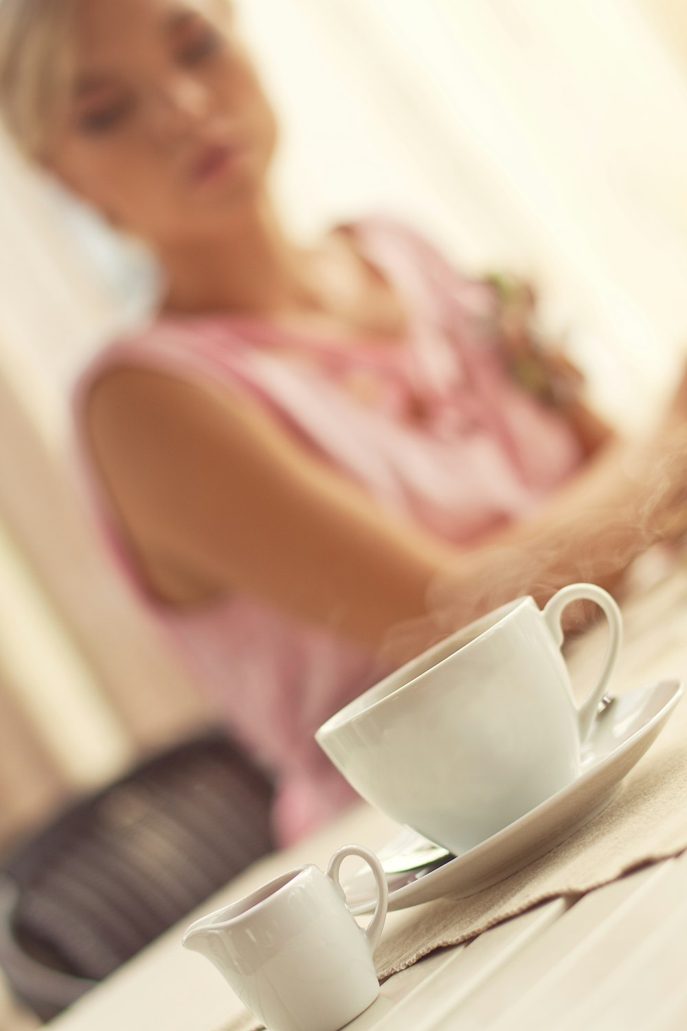 woman wearing pink sleeveless blouse sitting near table and white ceramic cup and saucer on table