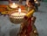 A beautifully decorated small figurine is holding a lit tealight candle. Around the figure, there are more delicate decorations and intricate patterns, including marigold flowers set on a colorful background. The ambiance is festive, warm, and inviting.