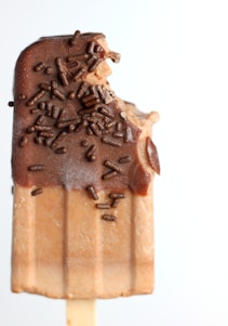 A popsicle with a chocolate coating and chocolate sprinkles, partially eaten with a bite taken out of the top.