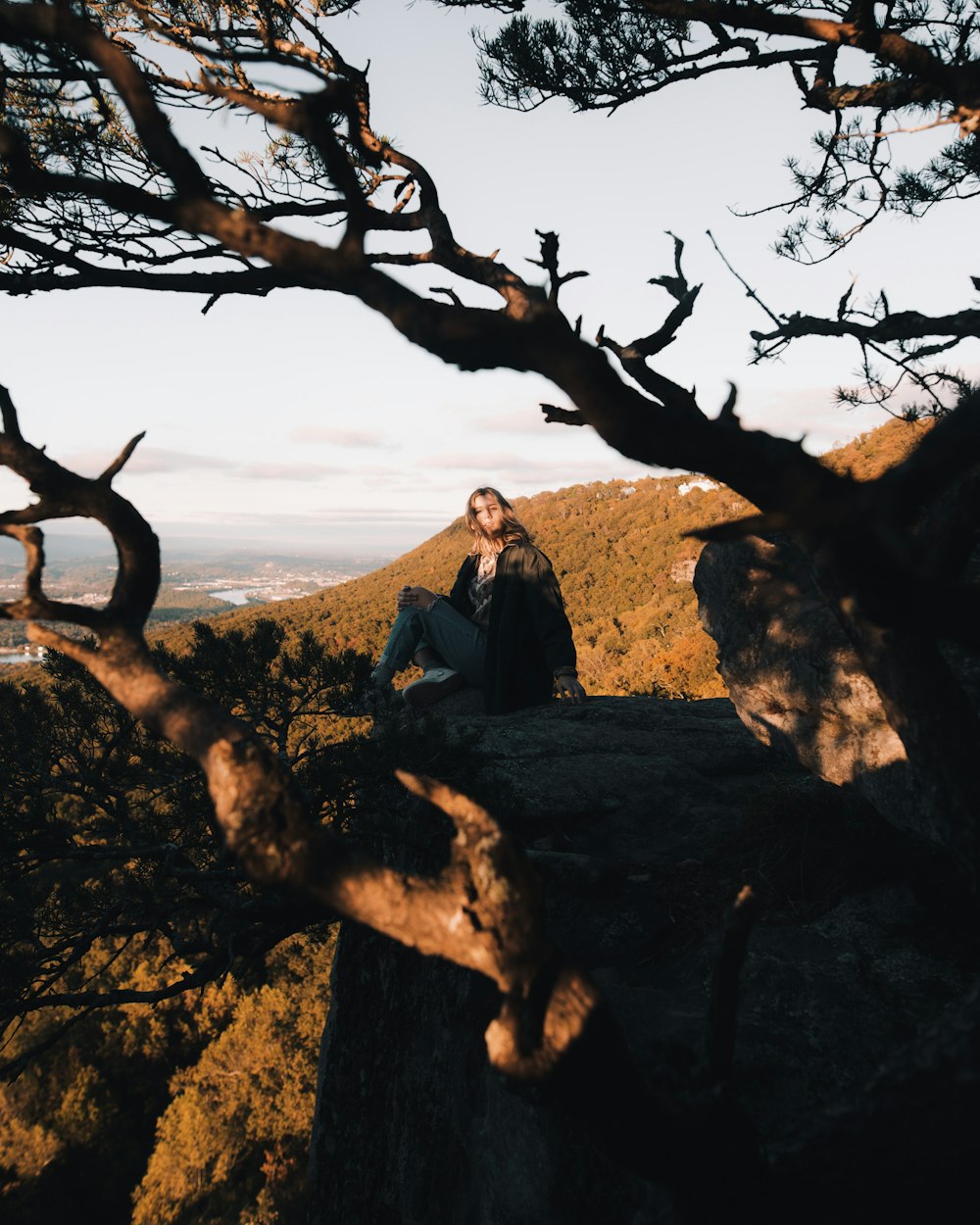 woman sitting on cliff near tree branches