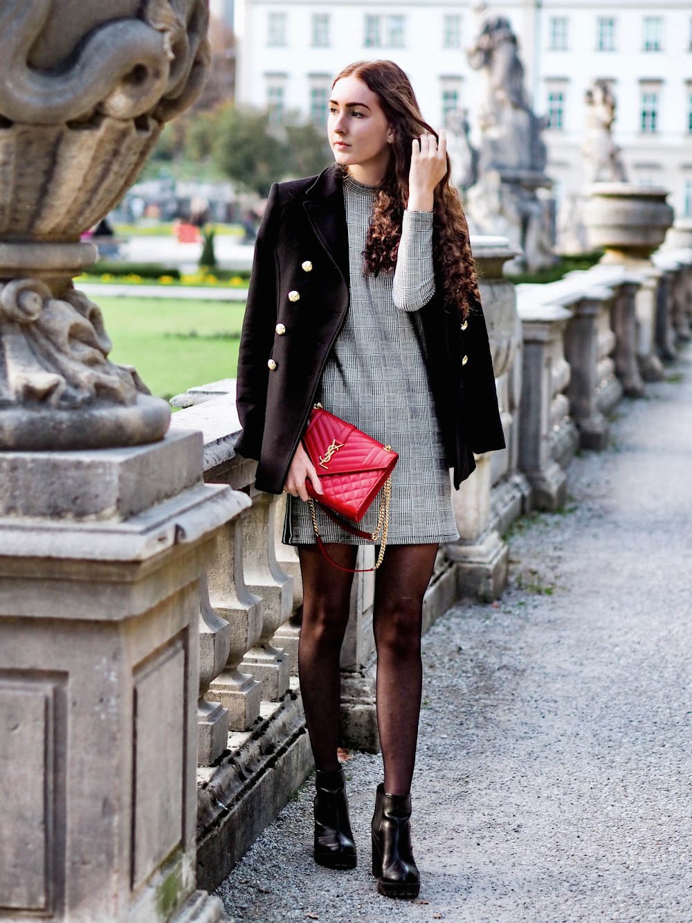 woman wearing gray long-sleeved dress with black blazer standing beside statue during daytime