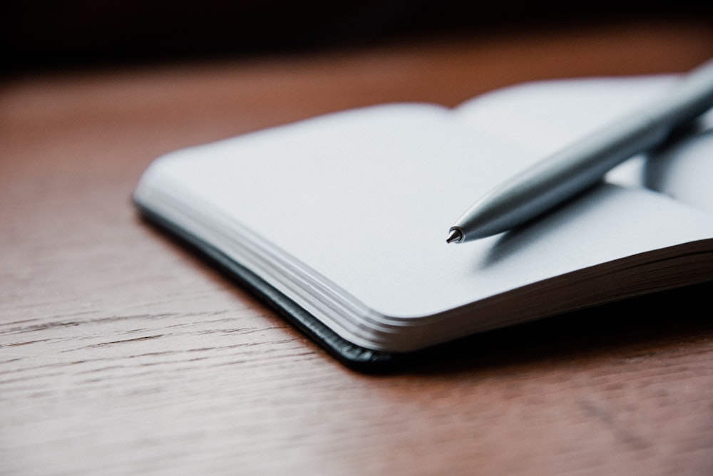 gray ballpoint pen on top of white book