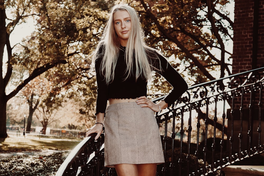 woman in black long-sleeved top and gray skirt leaning on black stair handrail