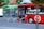 A bright red city bus with advertising for free Wi-Fi powered by a telecommunications company drives along a street. The bus appears to be in motion, and partially obscured by a tree. The background is slightly blurred, indicating speed. The word 'CROWN' is displayed on the bus’s digital sign.