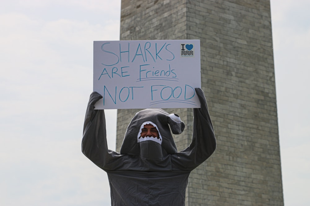 person wearing shark costume holding sharks are friends not food signage