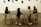 Four young children are interacting around a long, rectangular table with a smooth surface. The setting includes a wooden floor and a wall decorated with silhouettes of kitchen utensils. Above the table, the text on the wall partially reads '... sowing soon'.