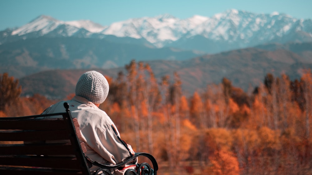 woman sitting on a bench looking at brown trees and snowy mountain