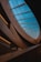 An interior architectural design featuring a large skylight with blue-tinted glass panels. The structure is characterized by smooth, curved wooden elements that create a modern and elegant aesthetic. The lighting is soft and focused, creating contrasting shadows and a warm ambiance.