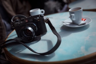 A warm-toned photograph of a vintage camera resting on a wooden table beside a travel journal and a cup of coffee.