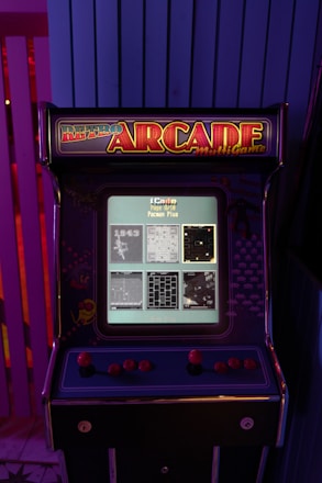 A vintage arcade machine with a display screen showing four game options. The cabinet is decorated with retro-themed artwork and vibrant colors, featuring a joystick and several buttons.
