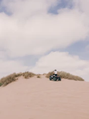 A rider on an ATV speeding along a sunlit sandy beach with ocean waves in the background.