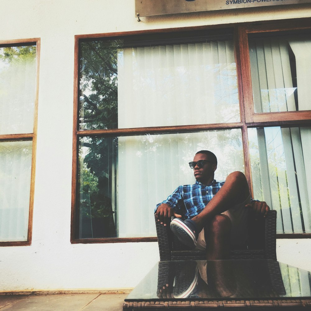 man in plaid shirt sittong on armchair beside glass window