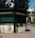 A green kiosk located in an urban outdoor setting, featuring closed rolling shutters. The signage reads 'Casino Sinaia' and 'Suveniruri' indicating it is a souvenir shop. Below the sign, there are decorative panels; one shows an ornate key and building, and another depicts a typewriter and papers with text that translates to 'This is where memories begin.' The scene is surrounded by paved walkways, trees, and partly visible buildings.