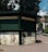 A green kiosk located in an urban outdoor setting, featuring closed rolling shutters. The signage reads 'Casino Sinaia' and 'Suveniruri' indicating it is a souvenir shop. Below the sign, there are decorative panels; one shows an ornate key and building, and another depicts a typewriter and papers with text that translates to 'This is where memories begin.' The scene is surrounded by paved walkways, trees, and partly visible buildings.