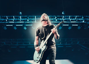 Close-up of a young artist passionately playing guitar under green lime stage lights.