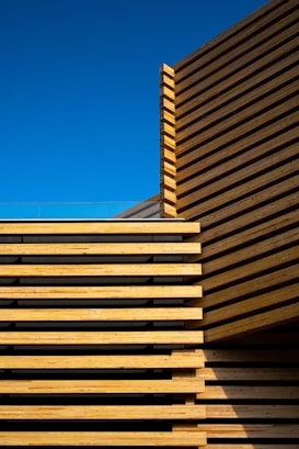Wooden architectural structure featuring an array of horizontal slats against a clear blue sky. The precise alignment of the wooden panels creates a modern, minimalist aesthetic.
