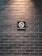 A dark brick wall features a prominently placed 'No Smoking' sign. The sign is centered and displays a cigarette with a red circle and slash, conveying the prohibition.