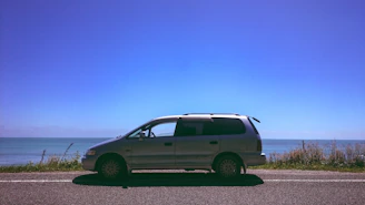 A premium minivan parked by a scenic coastal road under a clear blue sky