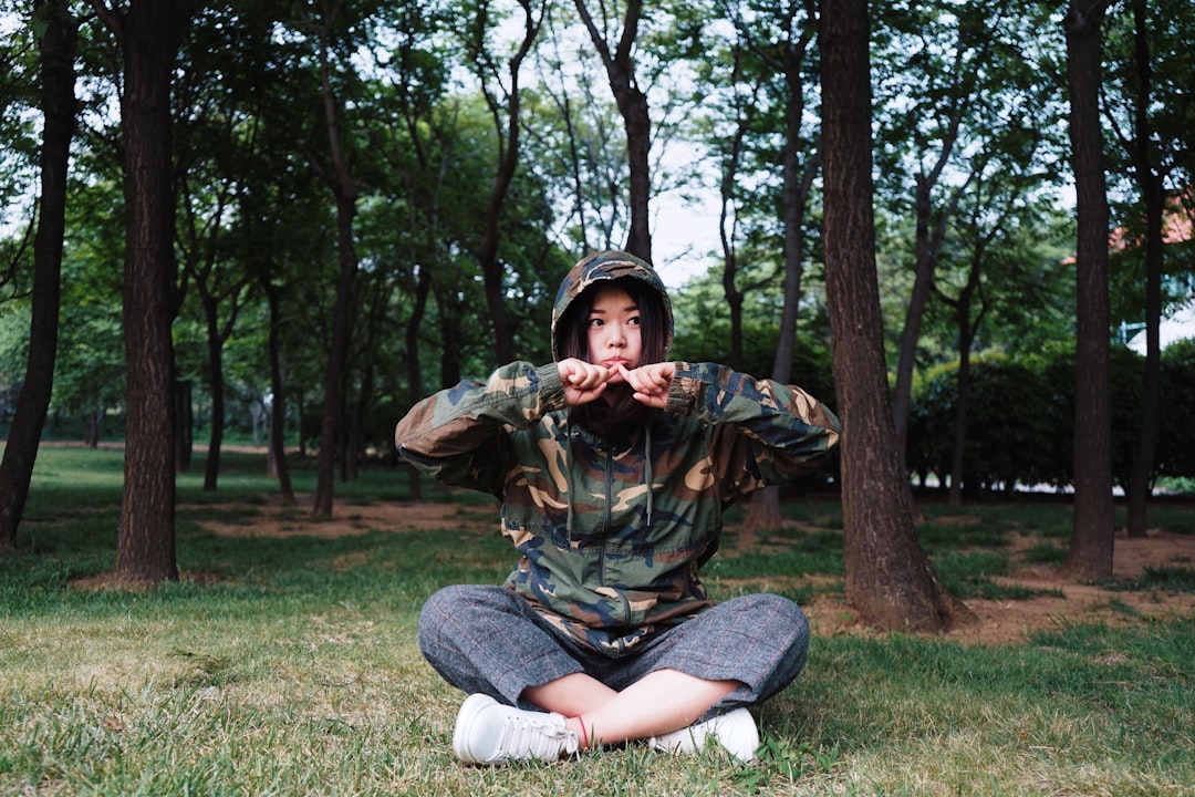 woman in camouflage hoodie sitting on grass near trees