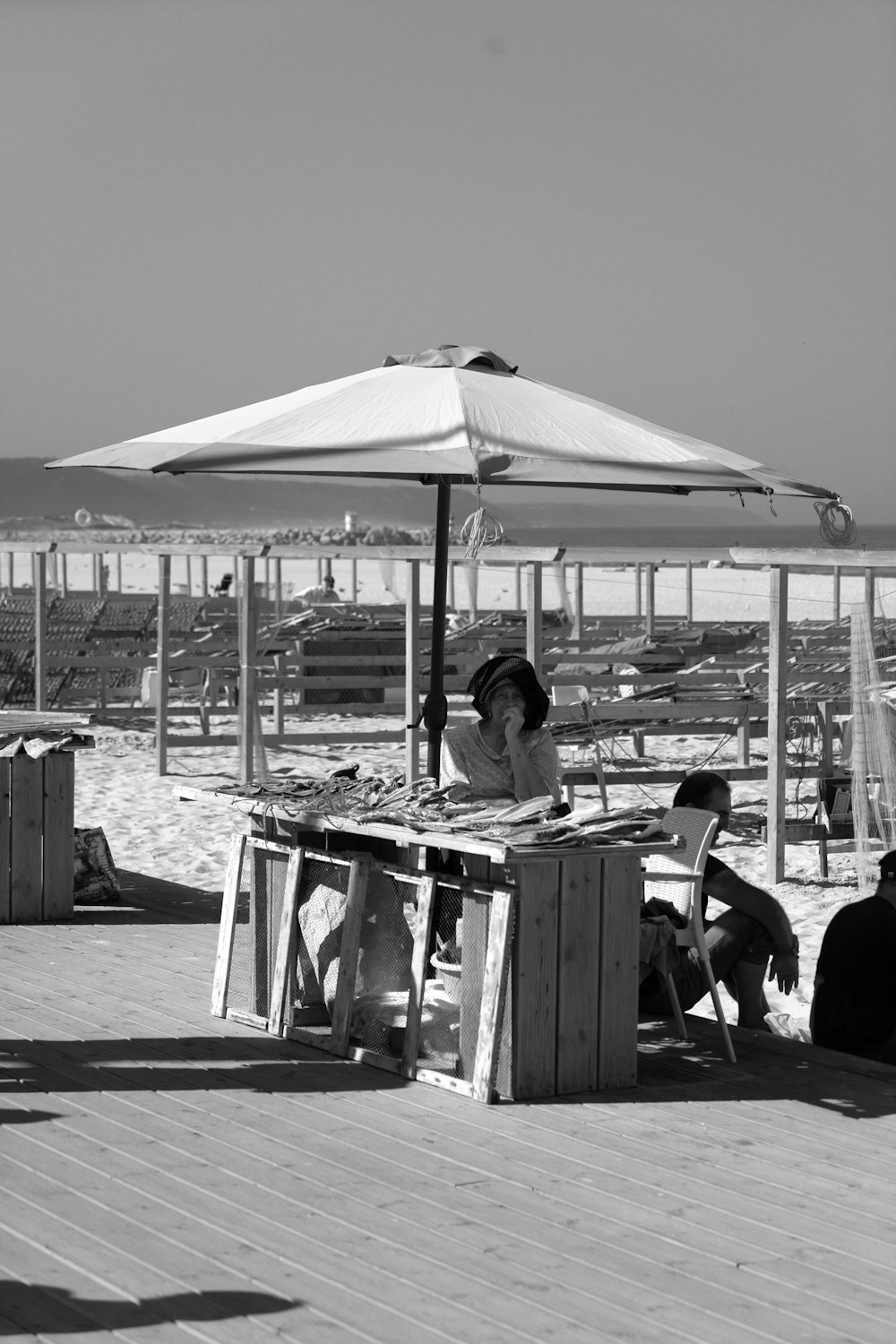grayscale photography of woman sitting under a beach umbrella