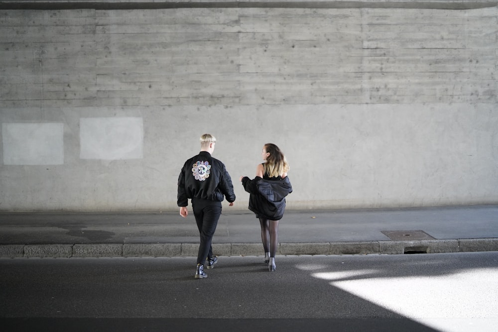 man wearing black and white jacket and black jeans walking on street with woman wearing black jacket