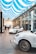 A modern showroom features two sleek white sports cars displayed under an elegant ceiling with blue and white striped fabric. The polished floor reflects the ambient light, and a railing separating the first and second floors adds a touch of architectural sophistication. A person stands near one of the cars, possibly an employee or customer, emphasizing the environment's professional and luxurious feel.