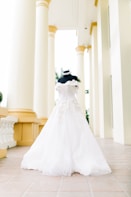 An elegant bridal gown in cream tones displayed on a minimalist mannequin against an off-white background.