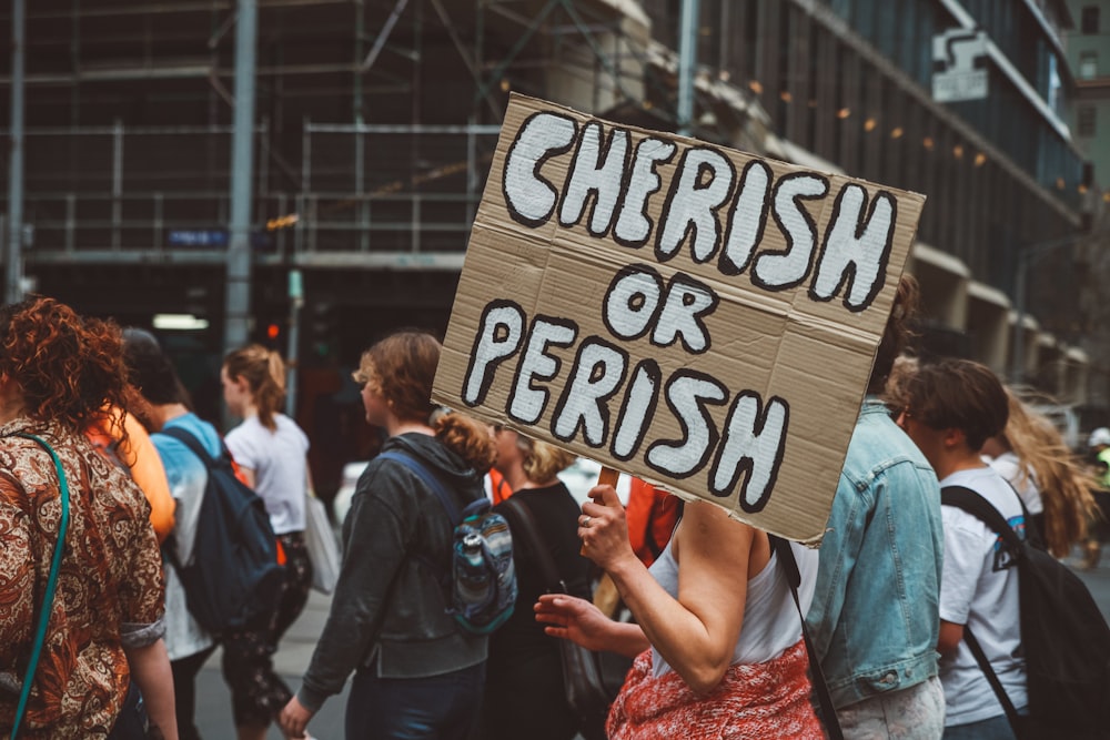 woman carrying cherish or perish-printed board sign in a rally