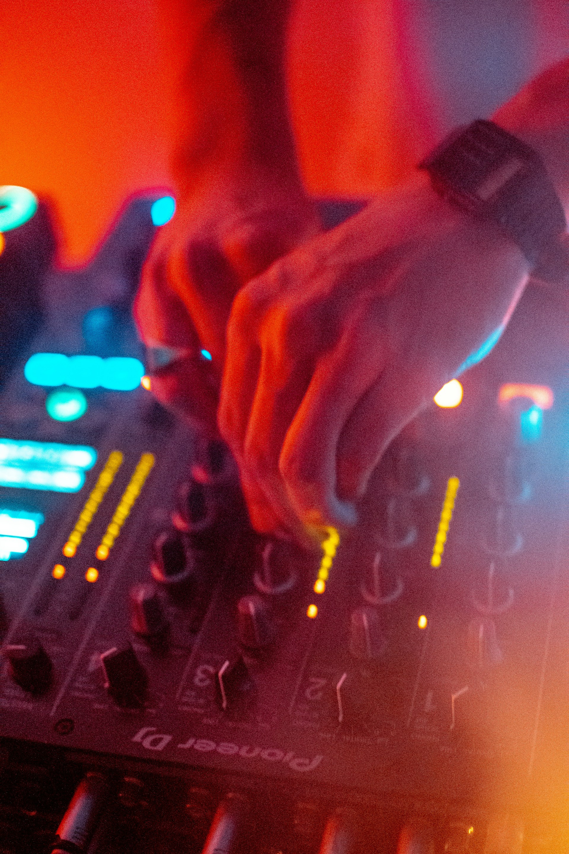 A close-up of a DJ's hand twisting knobs on a mixer, bathed in red and blue lights, evoking the intense energy of a dark techno rave.