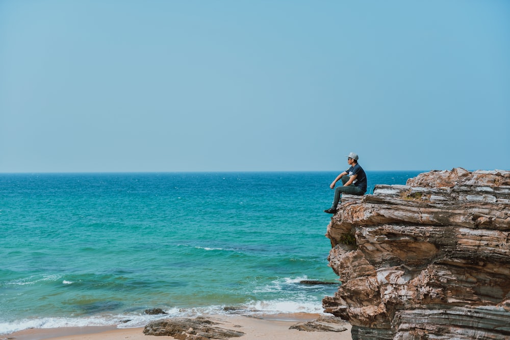 man sitting on cliff at beach