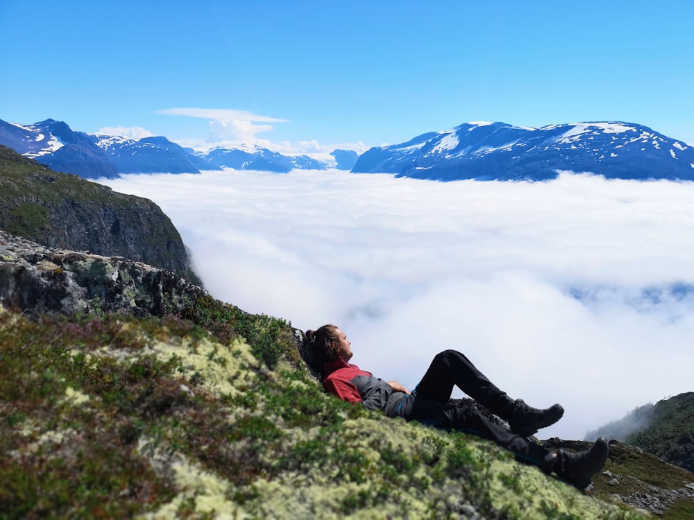 man lying on grass mountain during day