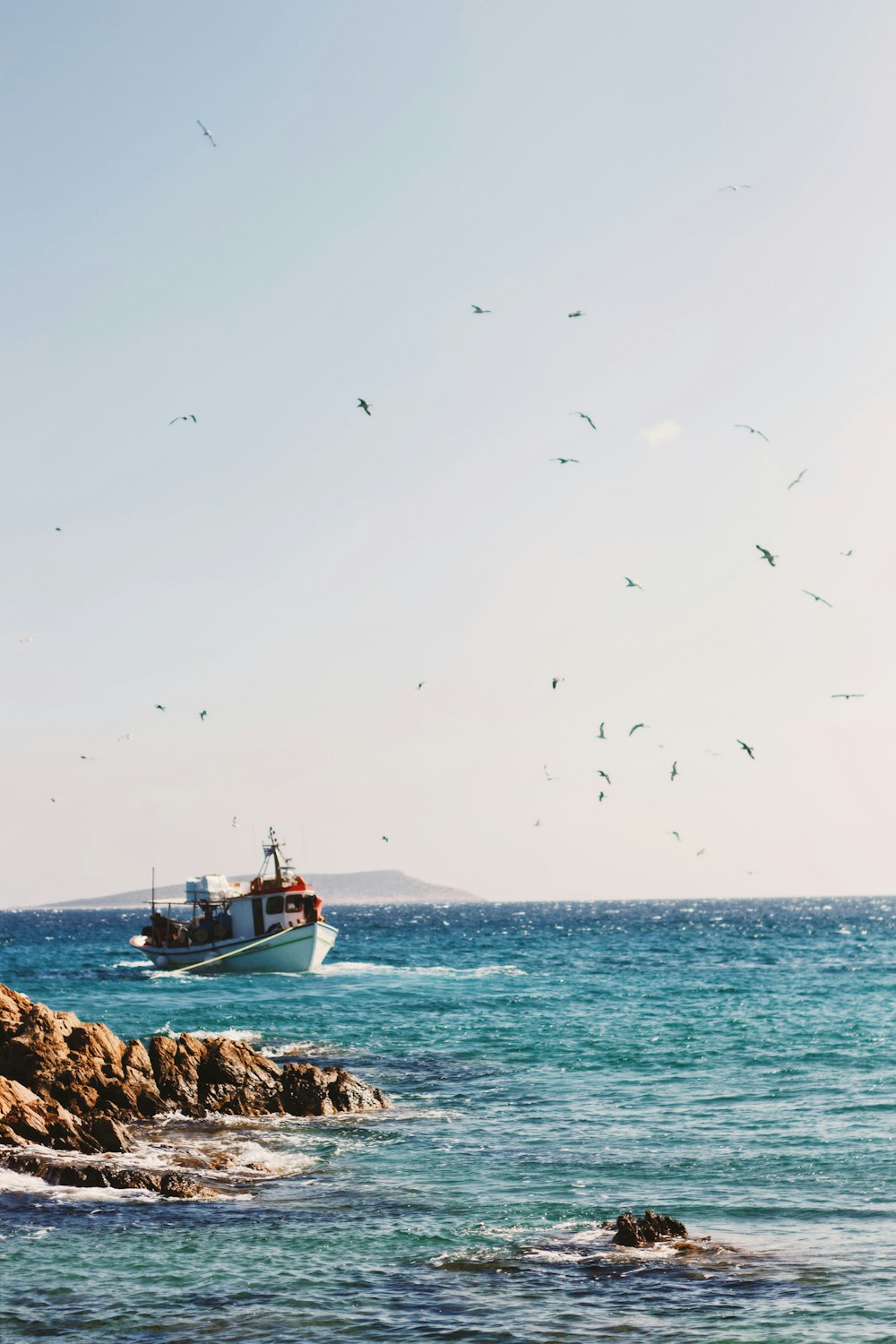 fishing vessel sails near rocks during daytime