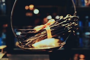 A bundle of dried vanilla beans tied together with an orange ribbon rests on a vintage scale. The background is softly blurred, creating a warm and cozy ambiance with bokeh lights.