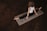 A person is practicing yoga on a mat in a dimly lit room with wooden floors. The person is wearing a white sleeveless top and black pants, sitting in a split position with hands on the mat, facing away. The mat has artistic designs.