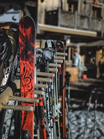 Rows of sturdy ski poles and helmets lined up on a wooden rack outside a ski shop