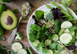 sliced broccoli and cucumber on plate with gray stainless steel fork near green bell pepper, snowpea, and avocado fruit