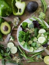 sliced broccoli and cucumber on plate with gray stainless steel fork near green bell pepper, snowpea, and avocado fruit