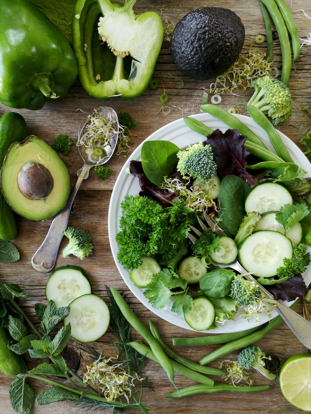 brócoli y pepino en rodajas en un plato con un tenedor de acero inoxidable gris cerca de pimiento verde, guisante y aguacate