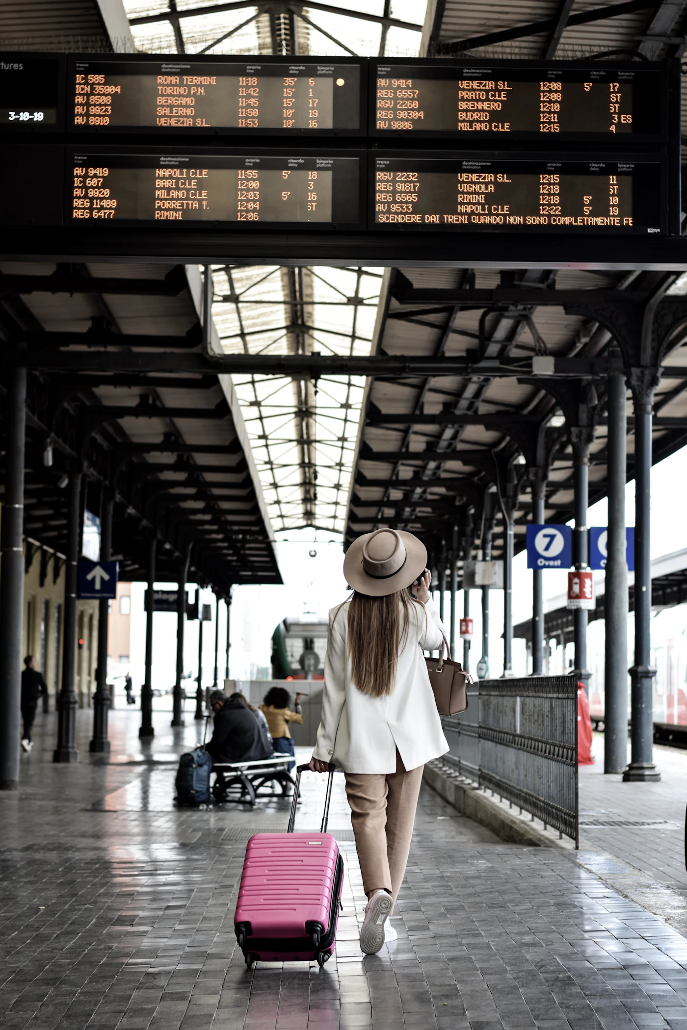 A traveler walking with rolling luggage beneath glowing departure boards on a covered platform, ready for the trip ahead