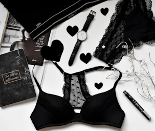 A stylish black cap and a sensual lingerie set laid out on a soft bedspread.